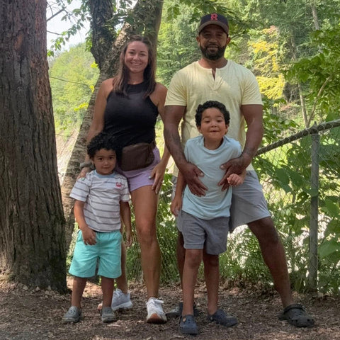 Family of four posing outdoors in a park with trees and greenery.